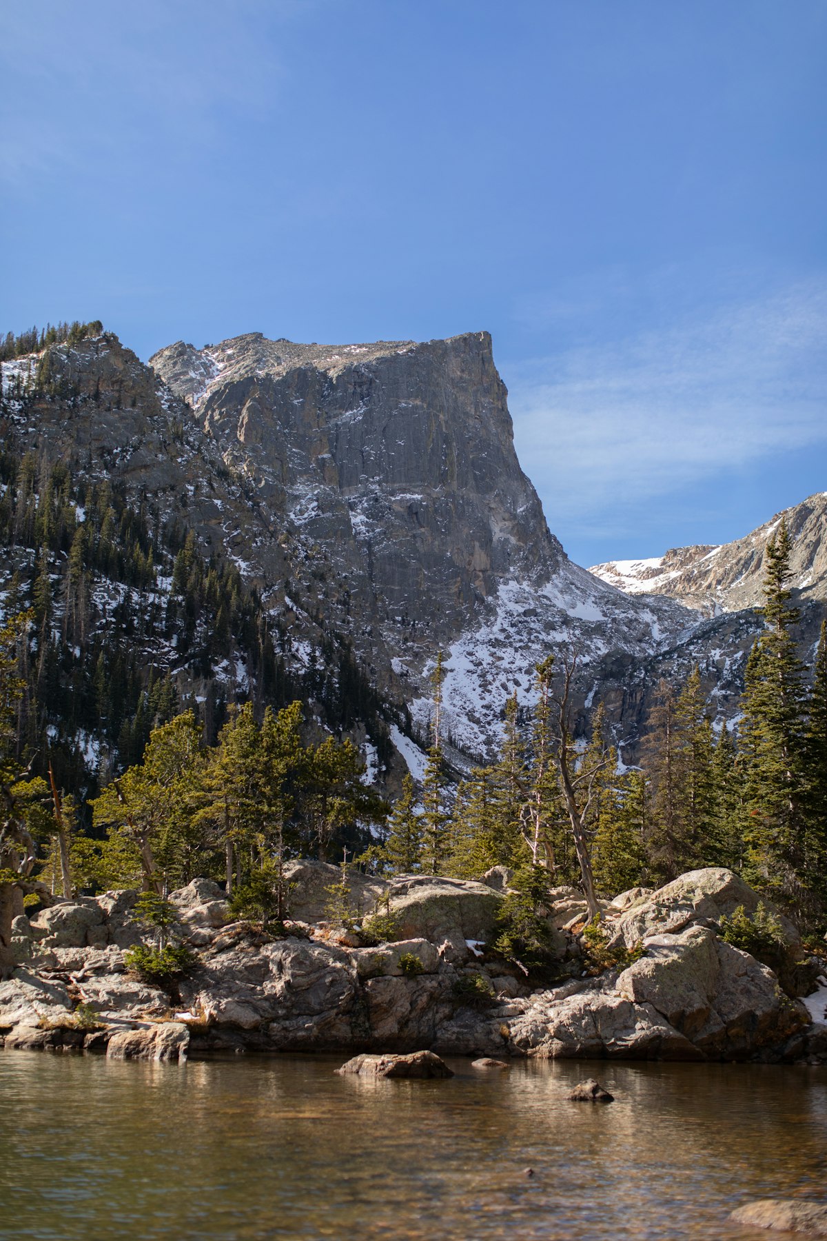 Snow-dusted cliffs, pine forest and an alpine lake in Rocky Mountain National Park